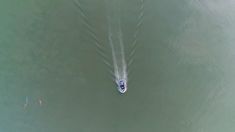 Top-down-aerial-of-a-fish-vessel-travelling-past-three-kayakers-in-a-sizable-expanse-of-open-water