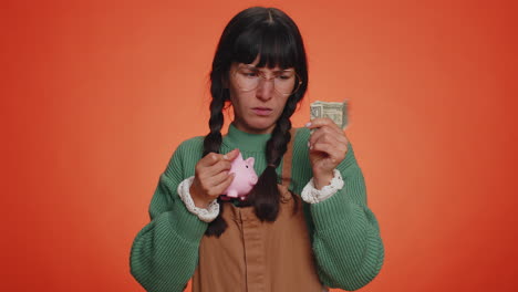 Poor-young-nerd-woman-holding-piggybank-and-one-dollar-banknote,-bankruptcy,-crisis,-poverty,-credit