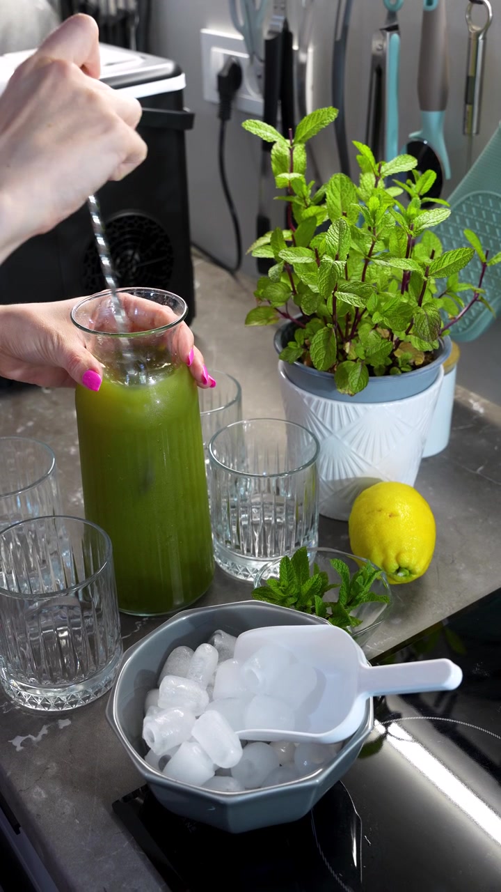 Yeşil naneli limonata, bir kase buz, taze limonlar ve nane bitkisinin yanında karıştırılıyor, dikey statik çekim.