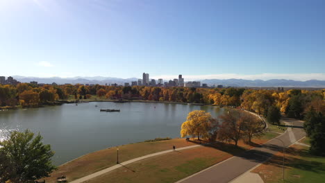 aerial shot of denver, colorado on a sunny day during fall with colorfull trees, mountains, skyscrapers and sunlight reflecting in a lake