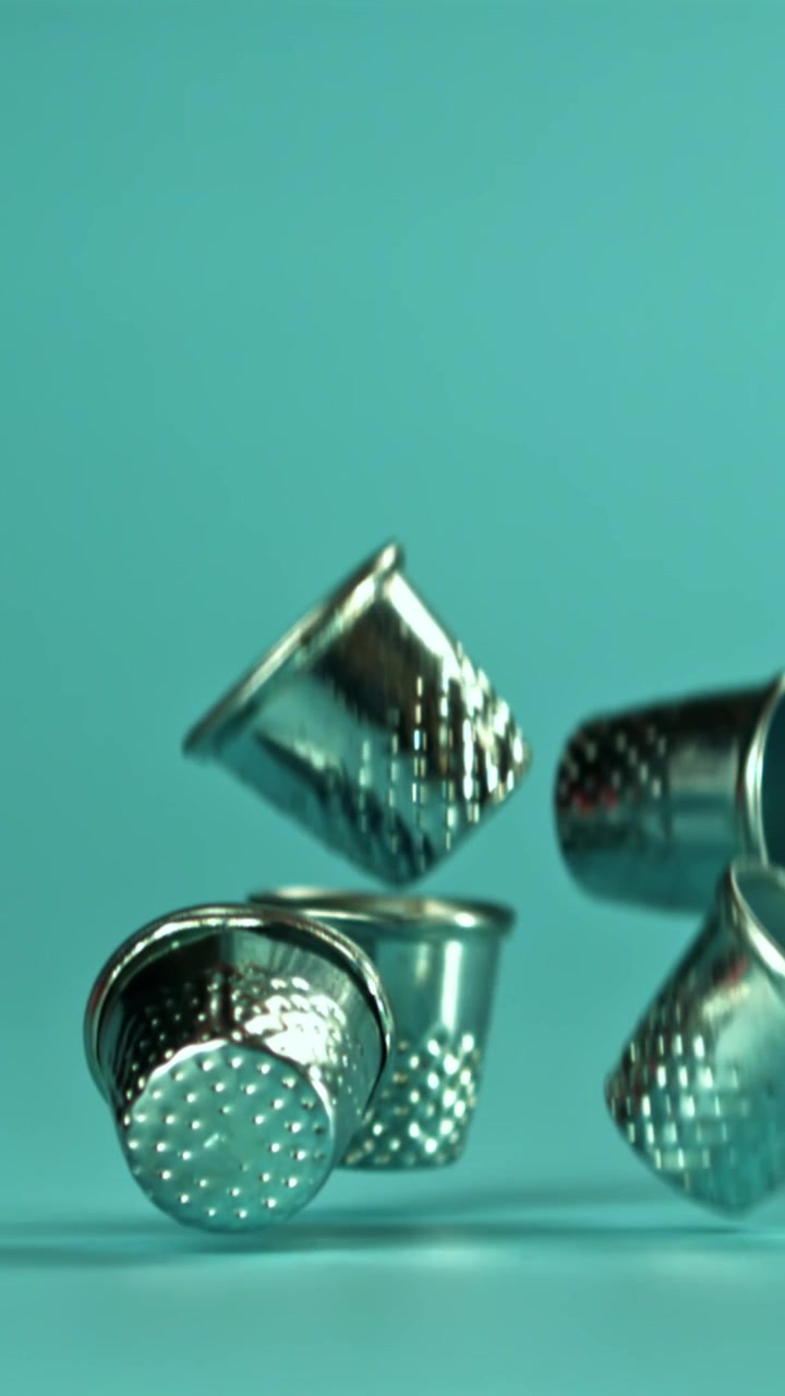 Metal Thimbles Falling in Slow Motion on a Teal Background