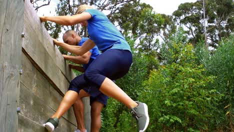 Couple-climbing-down-a-wooden-wall-during-obstacle-course