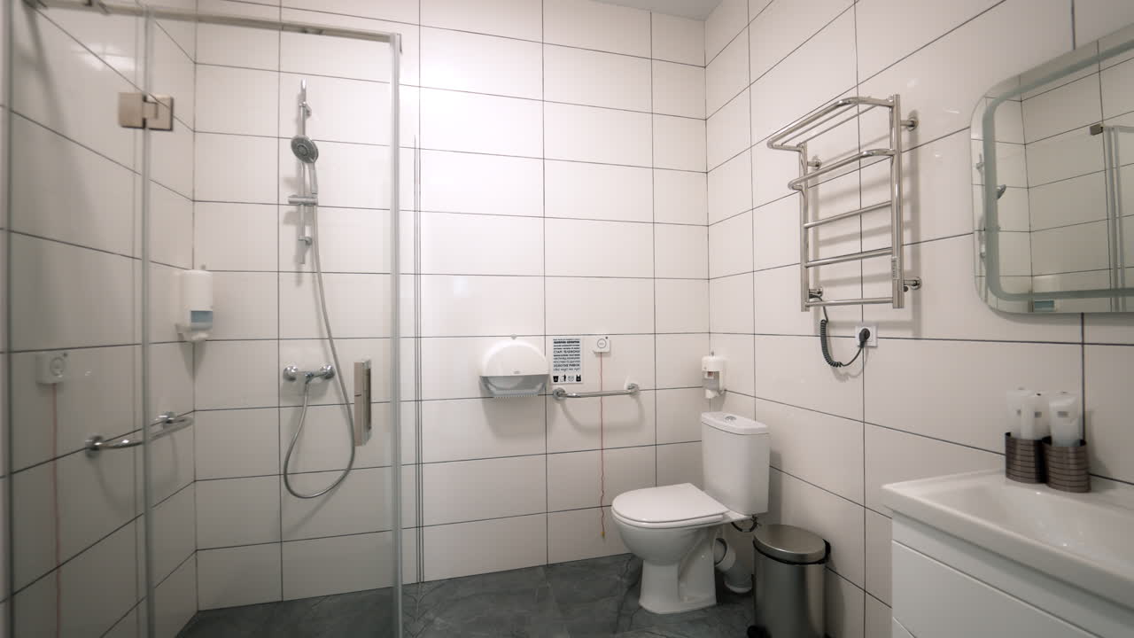 Kyiv, Ukraine, 3. august 2025: Tilgængeligt hvidt flisebelagt badeværelse på en moderne lægeklinik. Rent hospitalsbadeværelse med hvide fliser, toilet, forkromet gribestang, opvarmet håndklædetørrer.