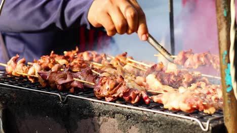 person turning skewered meat over a grill