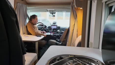 anciano trabajando en una laptop en autocaravana, gente caminando afuera bajo la lluvia, concepto de nómada digital