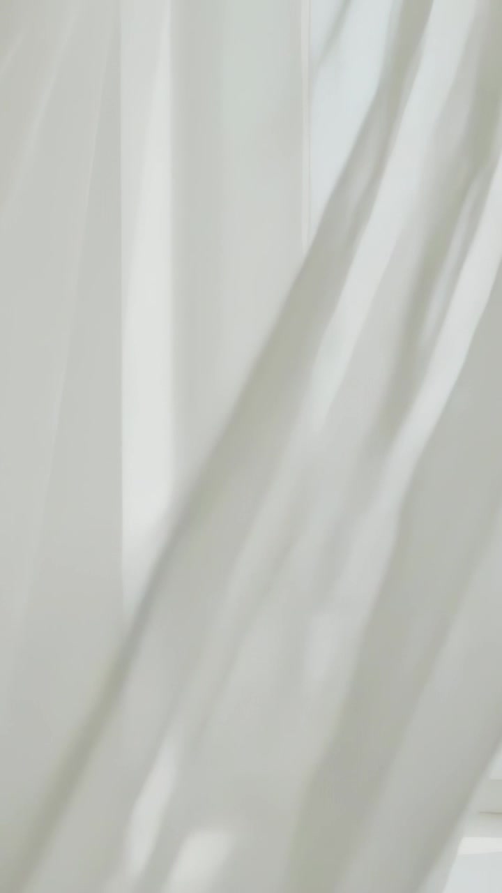 Vertical video: Billowing sheer curtain revealing window frame and hinge by gentle breeze in room