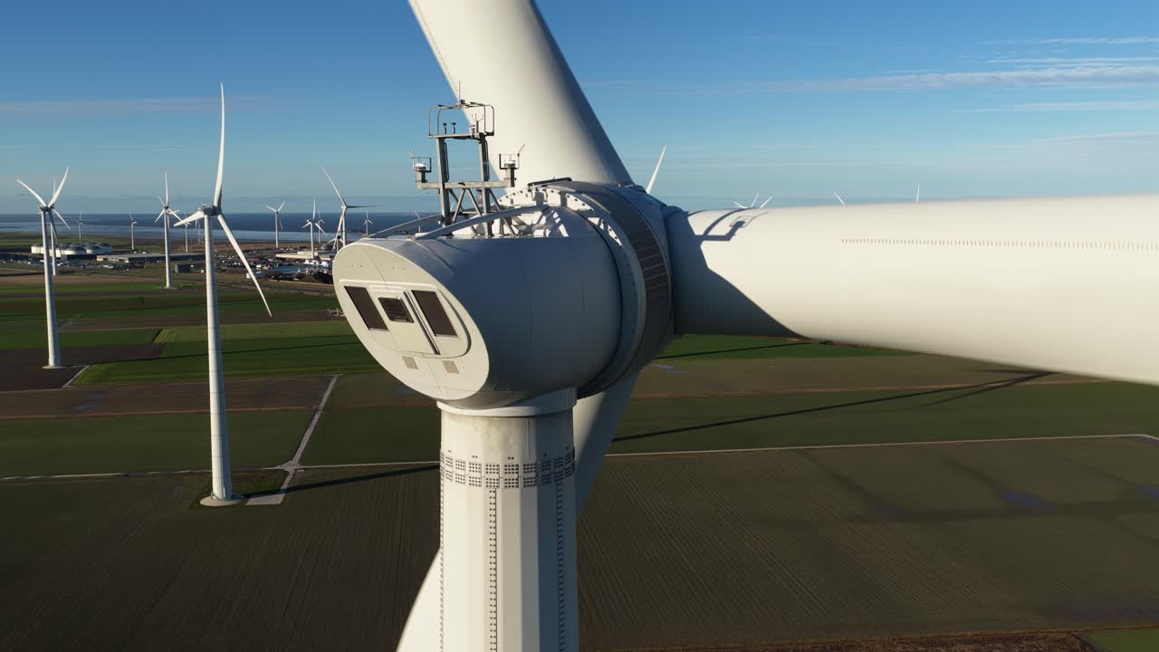 Close-up aerial video showing a spinning wind turbine directly in front of a major data center in Eemshaven, Netherlands. Highlights clean, sustainable power and green IT infrastructure