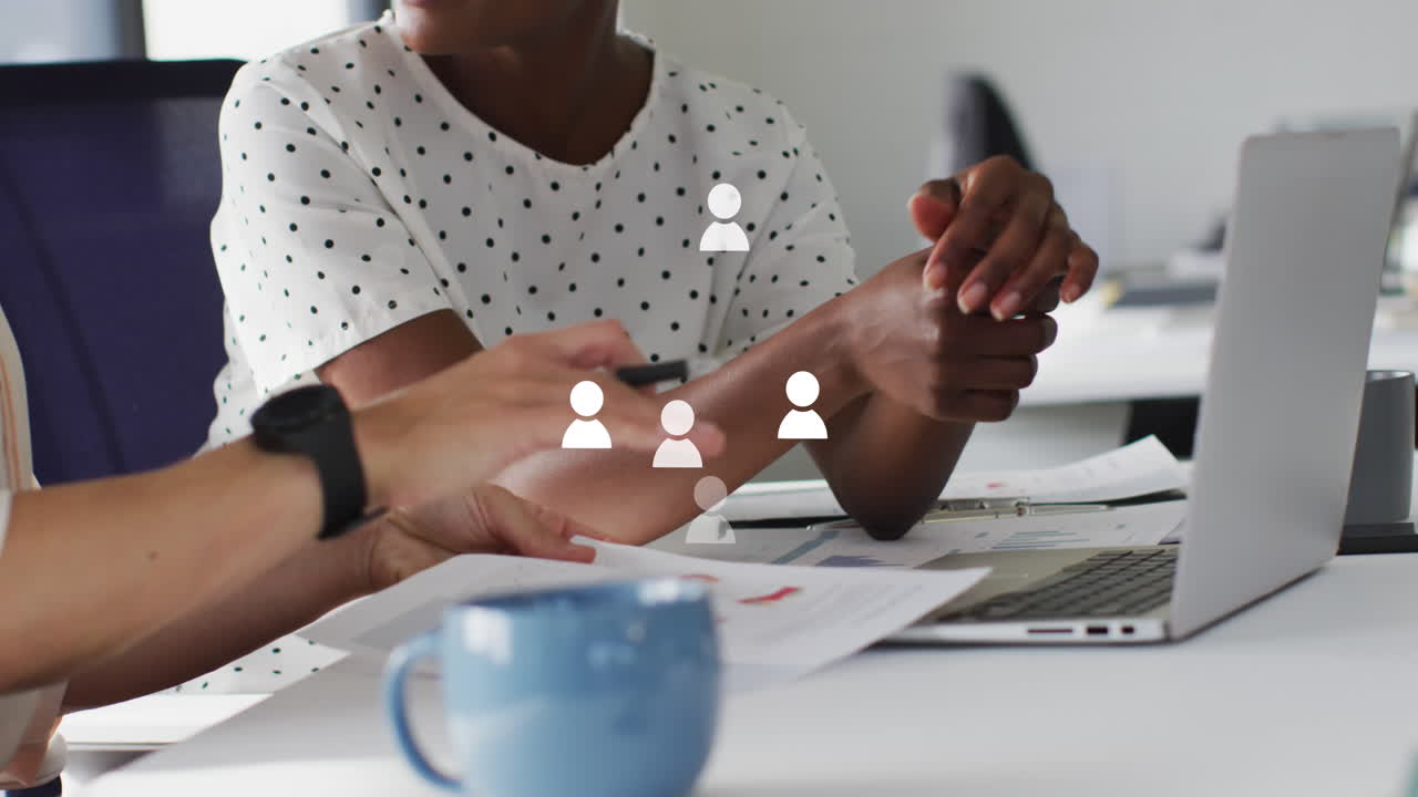Animation of profile icons floating against two diverse women discussing at office
