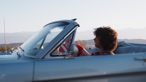 Happy-female-friends-driving-in-convertible,-one-raising-arm