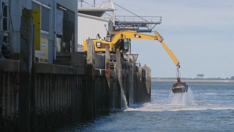 excavadora amarilla trabajando en una plataforma sacando cosas del mar en cámara lenta