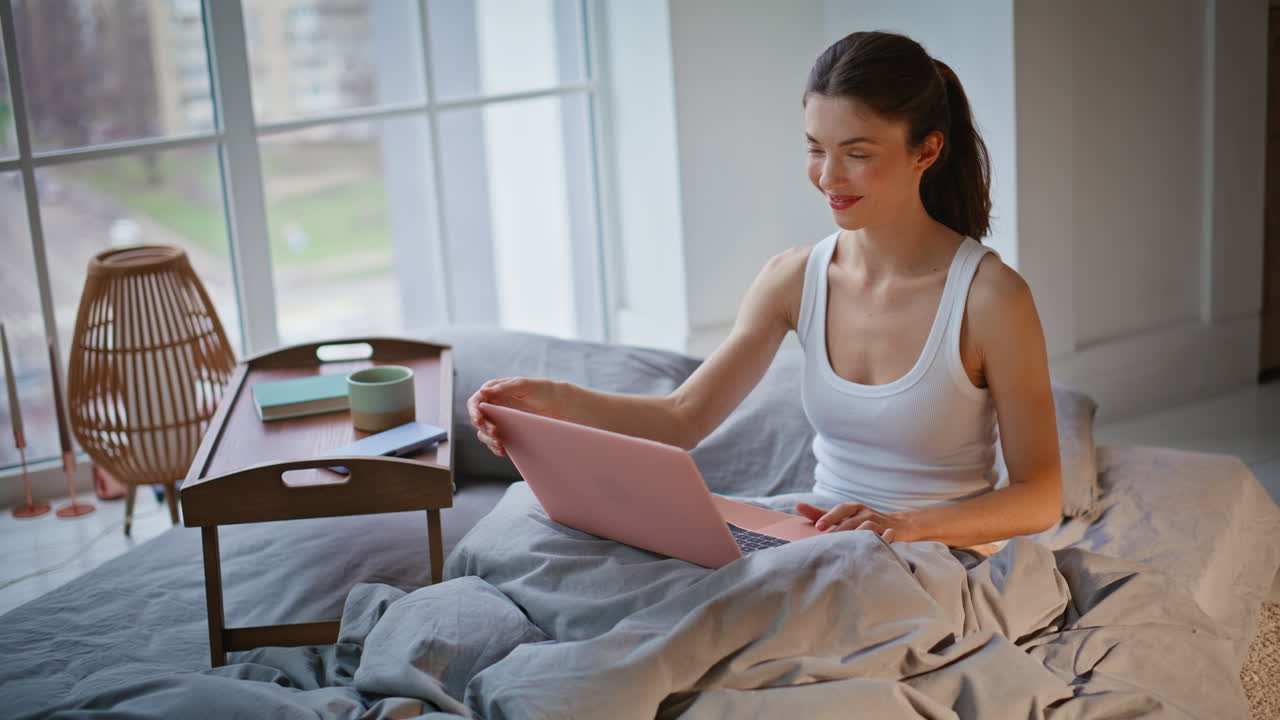 Donna d'affari sveglia che lavora al laptop a letto la mattina presto. Donna che chiude il computer.