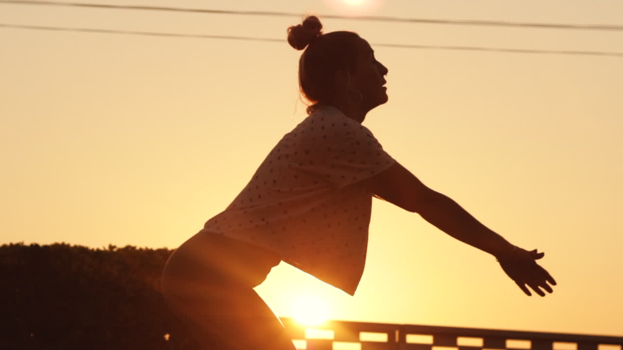 Silhouette of young woman does sun salutation yoga pose at sunrise in slow motion with a strong sun backlight