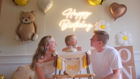 a couple celebrates with laughter and a birtay cake for their baby a joyful family scene features a man and woman celebrating with their baby they share smiles beside a high chair enjoying a birtay cake marking a special moment
