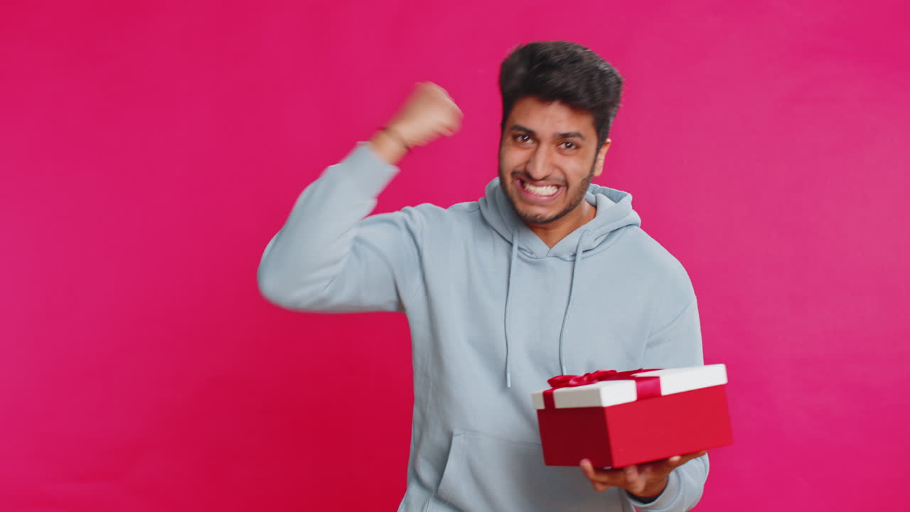 Excited indian man receiving gift with red bow opening box celebrating surprise present happiness