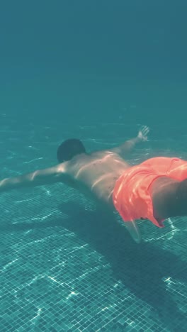 un joven nada bajo el agua en una piscina.
