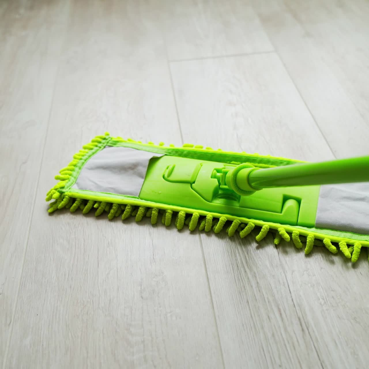 Modern mop on the wooden floor background. Cleaning the parquet floor by a green microfiber brush. Housekeeping routine.