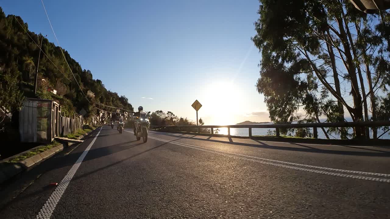 Group of adventure bikers riding on asphalt road near the sea at sunset. Chilean Patagonia