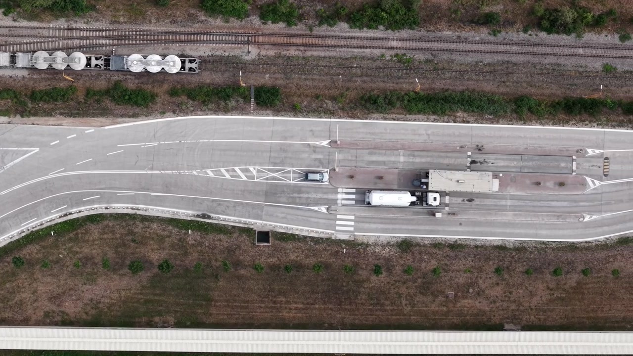 An aerial view showcases a bustling logistics hub where a freight train and trucks navigate a complex road and rail network, highlighting modern transportation efficiency.