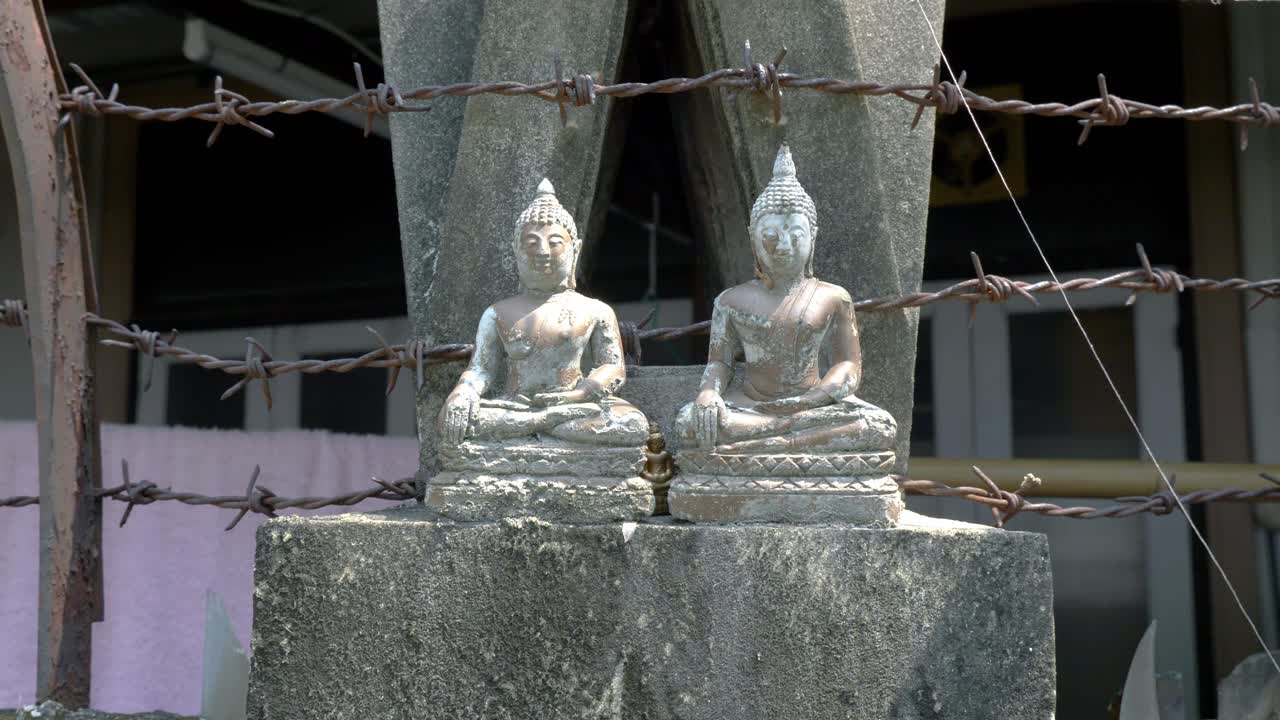 dos pequeñas estatuas de piedra de buda sentado en meditación con alambre de púas en segundo plano.