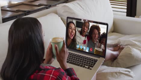 african american woman holding a coffee cup having a video call on laptop sitting on couch at home