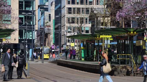people walk by tram station at st. peter’s square in manchester on busy spring day