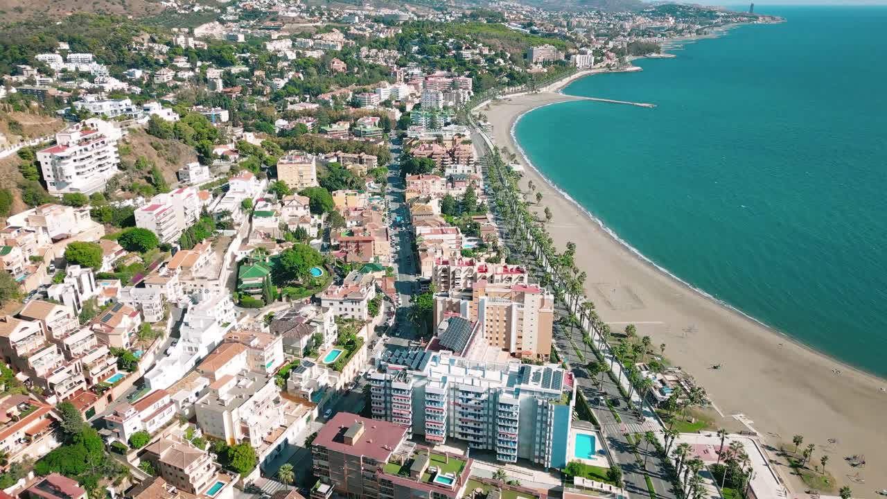 Aerial descent above La Caleta to Playa de la Malagueta, Málaga, Spain. Beautiful Mediterranean coastline destination in warm, calm summer light