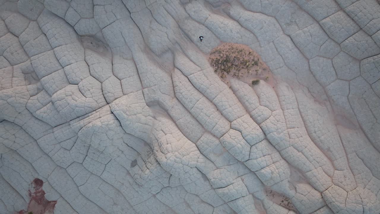 A top-down drone shot revealing the unique sandstone rock features of White Pocket Arizona surrounded by sandy desert and blue skies at blue hour