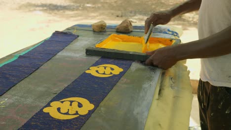 local african man printing with paint on handmade kente fabrics in ghana