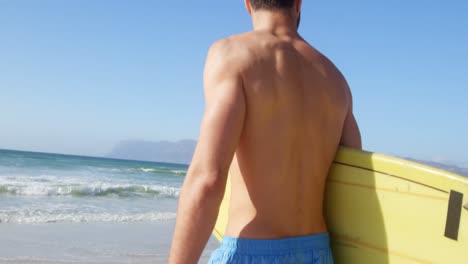 surfista masculino de pie con una tabla de surf en la playa 4k