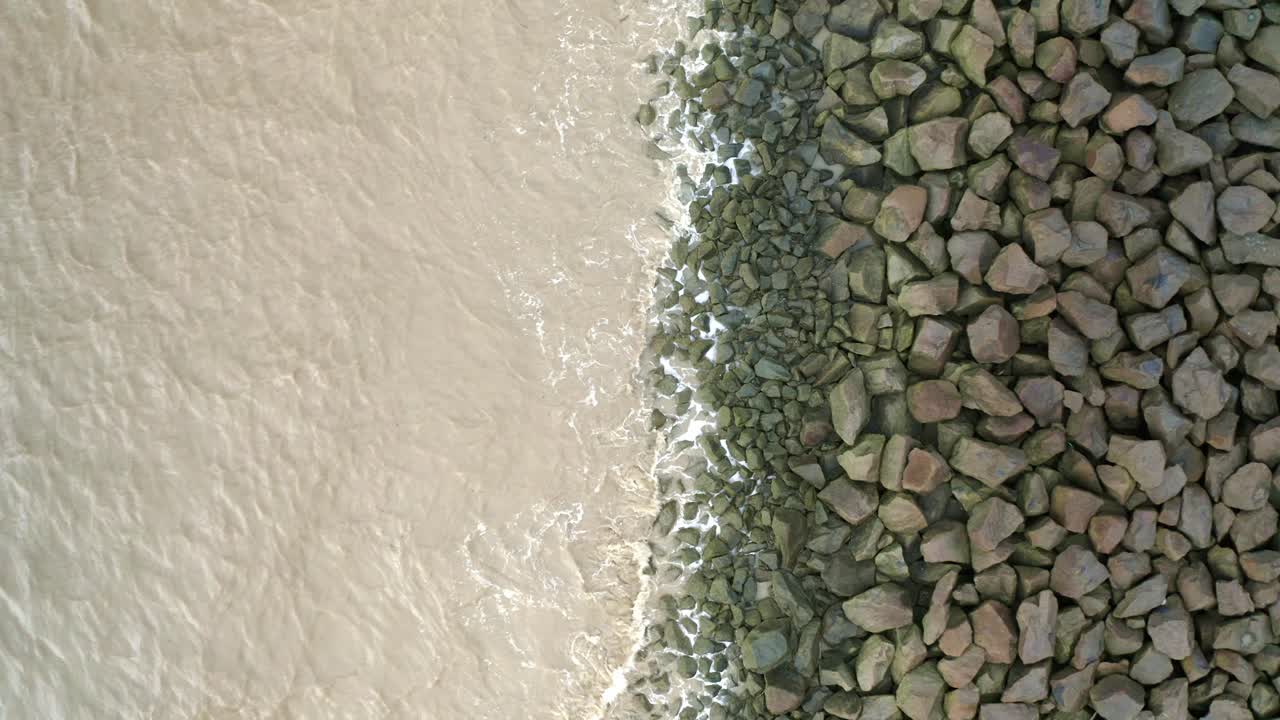 Onde marine che si infrangono sulle rocce di una diga marittima, ripresa aerea con drone in discesa