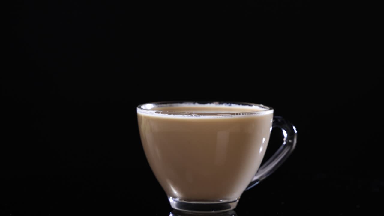 A glass cup filled with coffee rotates smoothly against a dark backdrop, highlighting its elegant design and rich color