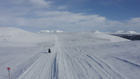 Imágenes-Aéreas-De-Un-Hombre-En-Una-Moto-De-Nieve-Pasando-A-Toda-Velocidad-Por-La-Cámara-En-Un-Paisaje-Invernal-En-Suecia