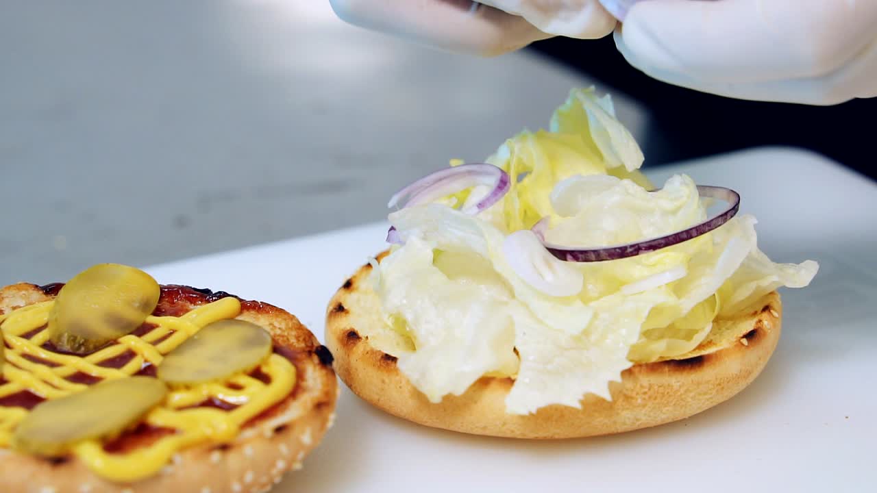 Preparing delicious burger. Chef putting onion rings while cooking hamburger. Process of making appetizing burger with vegetables. Fast food. Close-up
