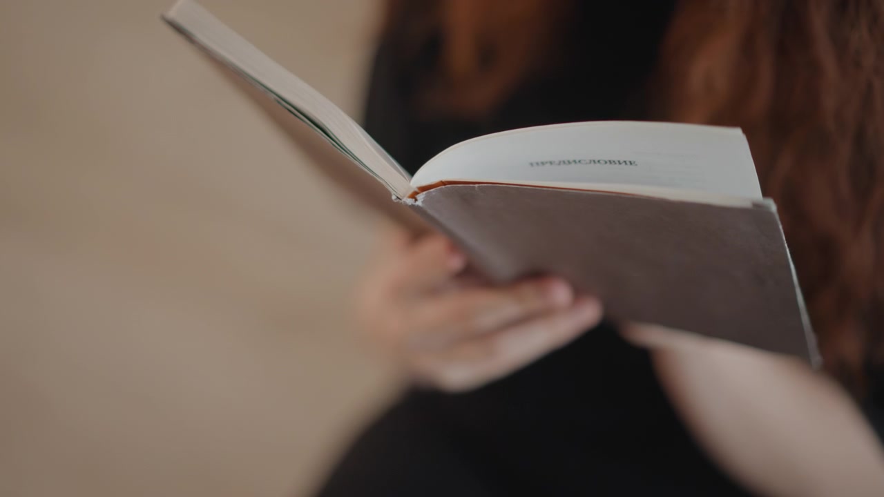 Primo piano di mani che tengono un libro tascabile aperto mentre le pagine si sfogliano verso l'alto, con una marcata curvatura delle pagine a mezz'aria e una leggera sfocatura di movimento che indica un'attiva azione di sfogliare le pagine