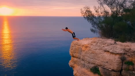 man cliff diving into the ocean at sunset