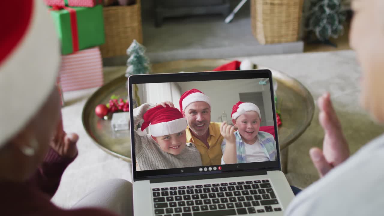 dos amigas mayores diversas que usan una computadora portátil para una videollamada de navidad con la familia en la pantalla