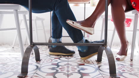 close up of a couple’s legs under the table at a restaurant, low angle