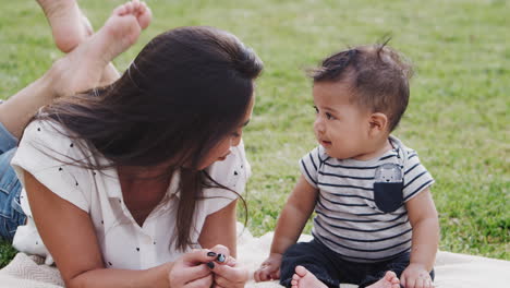 Millennial-Hispanic-mother-lying-on-the-grass-in-the-park-talking-to-her-baby-boy,-close-up