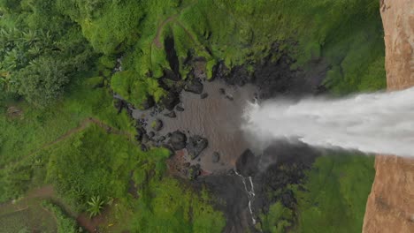 a moving forward aerial birds eye view shot of a waterfall in rural uganda plunging over the edge of a cliff into a deep pool