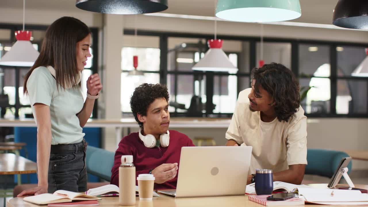 African American peers sitting at study table, man pointing at laptop with headset, doing project