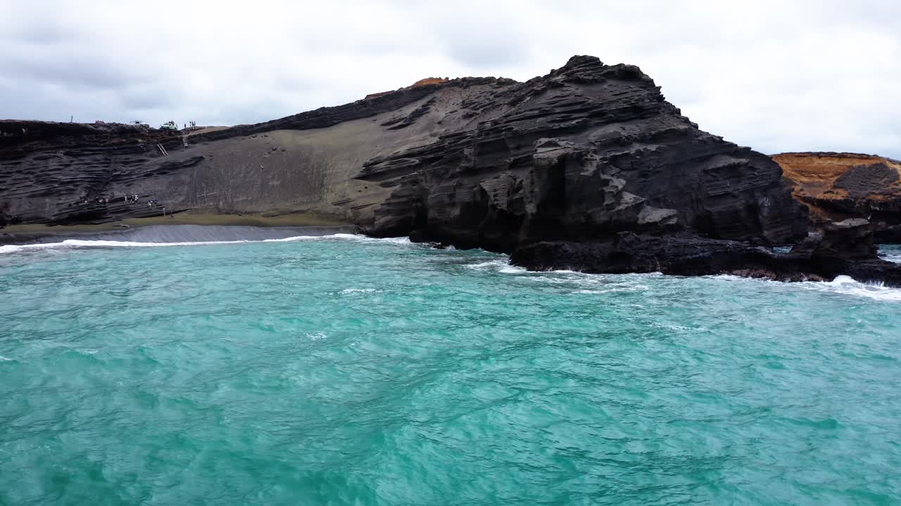 Powerful turquoise ocean waves collide with jagged volcanic cliffs and a striking black sand beach, highlighting the raw force of nature and dramatic coastal scenery.