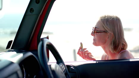 young caucasian woman applies lipstick in a car on a road trip