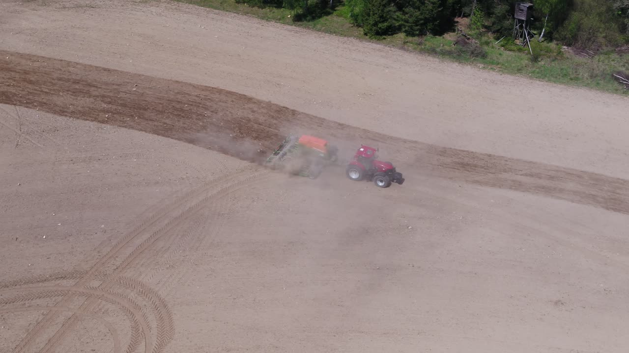 Aerial zoom in tracking a red tractor plowing farmland close to a green forest in Prague