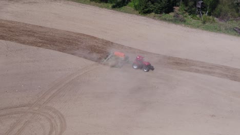 aerial zoom in tracking a red tractor plowing farmland close to a green forest in prague