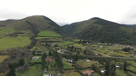 Green-grass-mountain-land-of-a-calm-living-area-in-Argentina,-Tafi-del-Valle,-on-a-cloudy-day,-truck-drone-shot-in-slow-motion