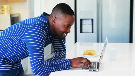 Hombre-Sonriente-Usando-Una-Computadora-Portátil-En-La-Cocina