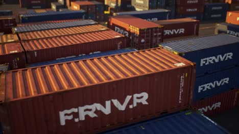 a large collection of shipping containers fills a vibrant port. various colors and sizes create a visually striking landscape under clear skies as cranes operate in the background.