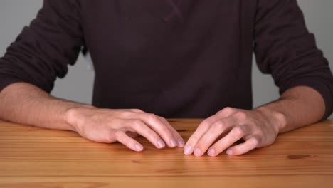 bored man sitting and tapping fingers on wooden table