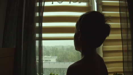 a silhouette of a little boy sitting by the window looking sadly outside