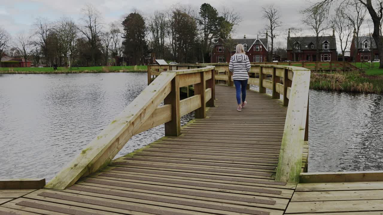 Una giovane donna cammina su un ponte in un parco locale